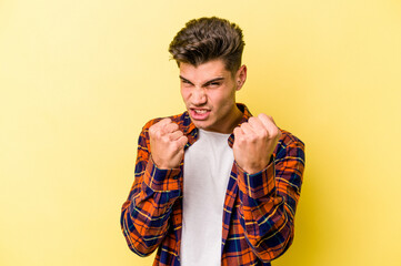 Young caucasian man isolated on yellow background showing fist to camera, aggressive facial...