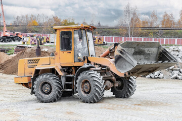 Fototapeta na wymiar The loader is transporting sand or gravel in the front bucket. Heavy construction equipment at a construction site. Transportation of bulk materials in a concrete plant.