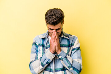 Young caucasian man isolated on yellow background praying, showing devotion, religious person...