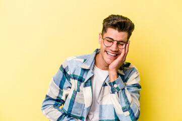 Fototapeta premium Young caucasian man isolated on yellow background laughs happily and has fun keeping hands on stomach.