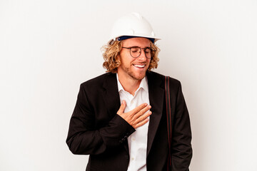Young architect caucasian man with helmet isolated on white background laughs out loudly keeping hand on chest.