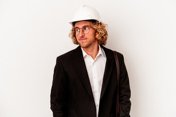 Young architect caucasian man with helmet isolated on white background looks aside smiling, cheerful and pleasant.
