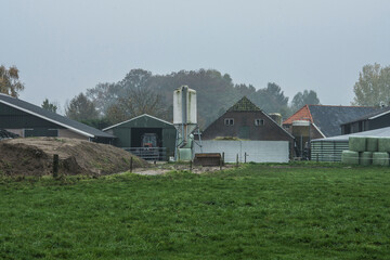 backsite of a farm with stables,  fodder silo, silage pile, green hay bales  and a tractor