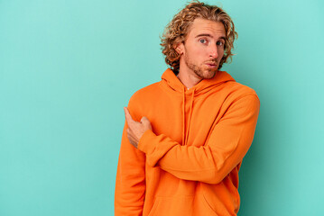 Fototapeta na wymiar Young caucasian man isolated on blue background smiling and pointing aside, showing something at blank space.