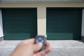 The hand tries to open the garage door with the remote control. Garage with two gates, double.
