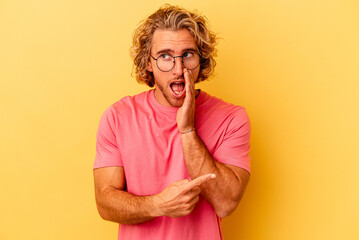 Young caucasian man isolated on yellow background saying a gossip, pointing to side reporting...