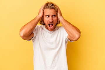 Young caucasian man isolated on yellow background covering ears with hands trying not to hear too loud sound.