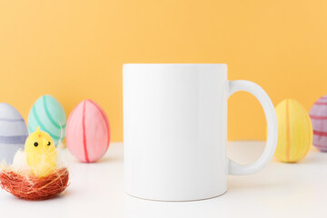 Easter coffee cup in white color standing on a wooden table with multi-colored eggs and a chicken. Mockup for logo application and copy space.