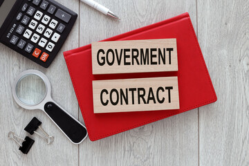 government contract text on wooden blocks on a notepad on a wooden background next to a calculator...