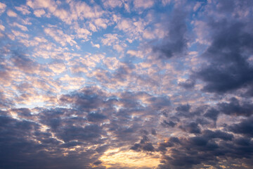 Evening blue sky with dark gray cumulus clouds around sunlight. Replacement texture.