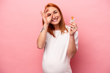 Young caucasian pregnant woman holding pacifier isolated on pink background excited keeping ok gesture on eye.