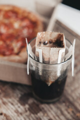 brewing coffee in a drip bag in a transparent glass, on a wooden background. Hot ground drip coffee, top view. Ground Ethiopian coffee in a reusable drip bag.