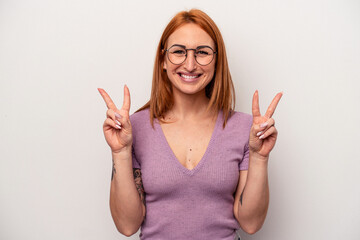 Young caucasian woman isolated on white background showing victory sign and smiling broadly.