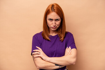 Young caucasian woman isolated on beige background frowning face in displeasure, keeps arms folded.
