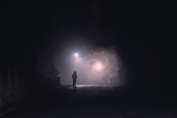 A science fiction, fantasy concept of a man looking at a glowing portal of light and stars against a street light on a spooky, foggy winters night