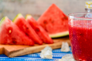 Normal view of part of a large glass with a cold watermelon smoothie and some triangles of delicious watermelon out of focus accompanying the background. Healthy, fresh and natural drink. 