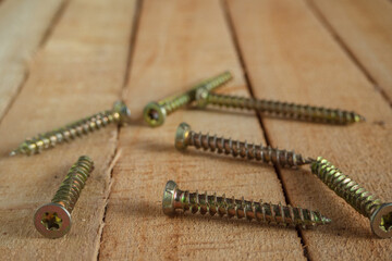 A group of gilded self-tapping screws randomly scattered on a wooden surface.