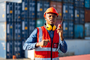 Container black man worker talking on walkie-talkie to Colleague control loading containers box at...