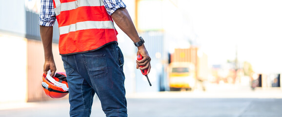 Container man worker holding walkie-talkie and safety hard hat helmet on hand at container...