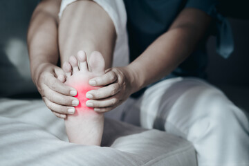 Woman sitting on the sofa and holding her foot suffering from foot pain with red highlight, massaging her painful foot, Healthcare and medical concept..