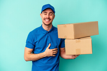 Young delivery caucasian man isolated on blue background laughing and having fun.