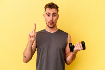 Young sport man holding a dumbbell isolated on yellow background having some great idea, concept of creativity.