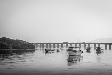 Barcos de pesca ancorados no mar e ao fundo uma ponte 