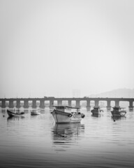 Barcos de pesca ancorados no mar e ao fundo uma ponte 