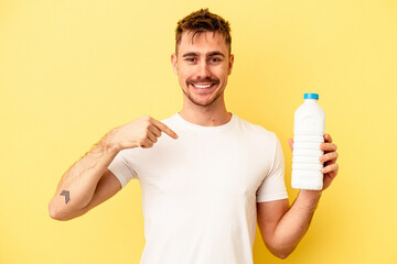 Young caucasian man holding a bottle of mil isolated on yellow background person pointing by hand to a shirt copy space, proud and confident