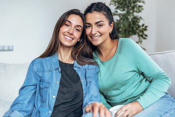 Two women friends taking a photo of themselves sitting on a couch at home.