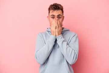 Young caucasian man isolated on pink background covering mouth with hands looking worried.