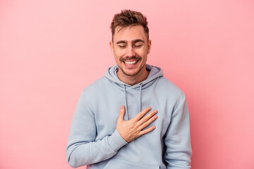 Young caucasian man isolated on pink background laughs out loudly keeping hand on chest.