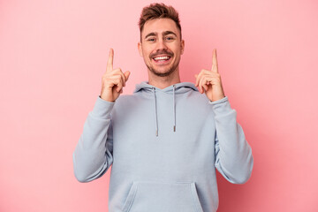 Young caucasian man isolated on pink background indicates with both fore fingers up showing a blank...