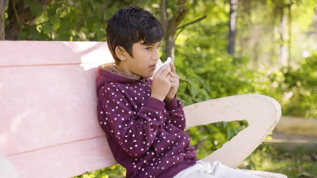 Young sick kid sneezing at park during winter - concept of seasonal winter illness, flu and infection