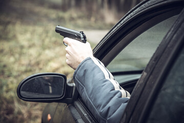A man with a gun driving a car, a man's hand with a gun in his hand leaned out of the car window