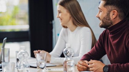 young businessman smiling near blurred woman and bottles with water in meeting room