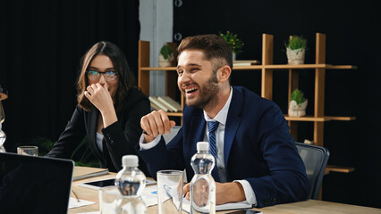 excited businessman laughing near woman in eyeglasses in office