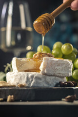 Organic homemade camembert or brie cheese on a wooden board with grapes and nuts and honey.