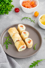 Fototapeta na wymiar Thin pancake rolls or crepes rolls with smoked salmon, cream cheese, cucumber and dill on a gray concrete background. Selective focus.