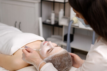 Obraz na płótnie Canvas Beautician applies the mask with a brush. Face peeling mask, spa beauty treatment, skincare.