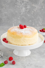 Japanese cotton cheesecake on a stand on a gray concrete background with fresh raspberries and powdered sugar on top. Selective focus, copy space.