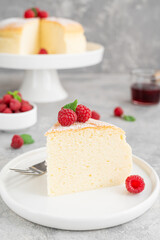 Japanese cotton cheesecake on a stand on a gray concrete background with fresh raspberries and powdered sugar on top. Selective focus, copy space.