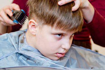 Naklejka premium Hairdressing saloon at home in quarantine conditions. Mother cuts boy's hair with scissors.