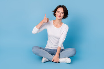 Photo of charming cute woman wear white shirt sitting legs crossed showing thumb up isolated blue...