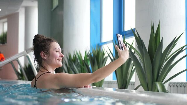 Young woman in a swimming pool taking photo of herself with cellphone.