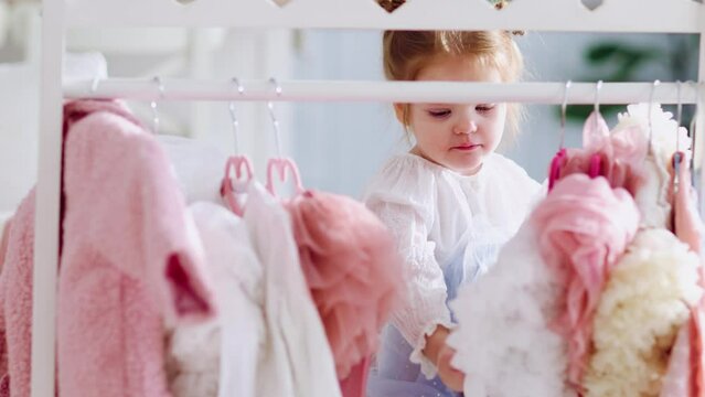 happy little girl hanging dresses on clothes rack stand in nursery room