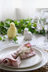 Fototapeta na wymiar Easter table setting with yellow chick, festive decorations, fresh flowers and eggs. Elegance dinner at home interior. Close up.