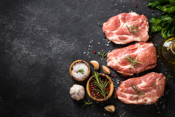 Fresh pork steaks with spices and hebs at black background. Top view with copy space.