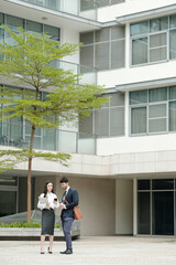 Business people standing outside the office building and discussing chart on smartphone screen