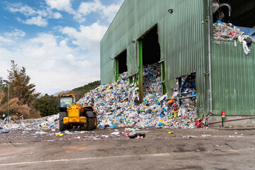Mechanical claw hand grabbing pile of mixed waste, deposited in the waste treatment plant depot, preparing it for separation. Waste disposal, management, reuse, recycle and recovery concept.